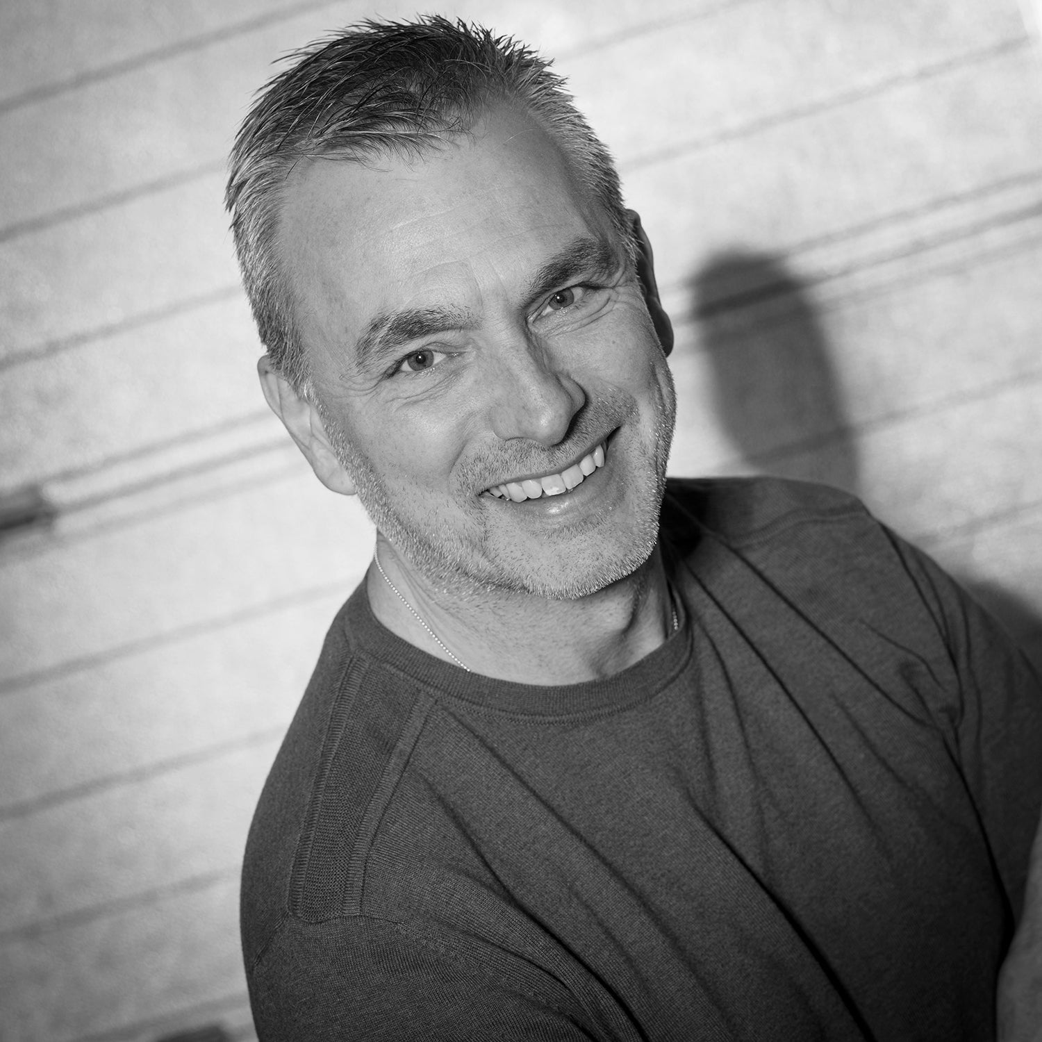 Mann mit kurzem Haar lächelt in die Kamera und trägt ein dunkles T-Shirt.