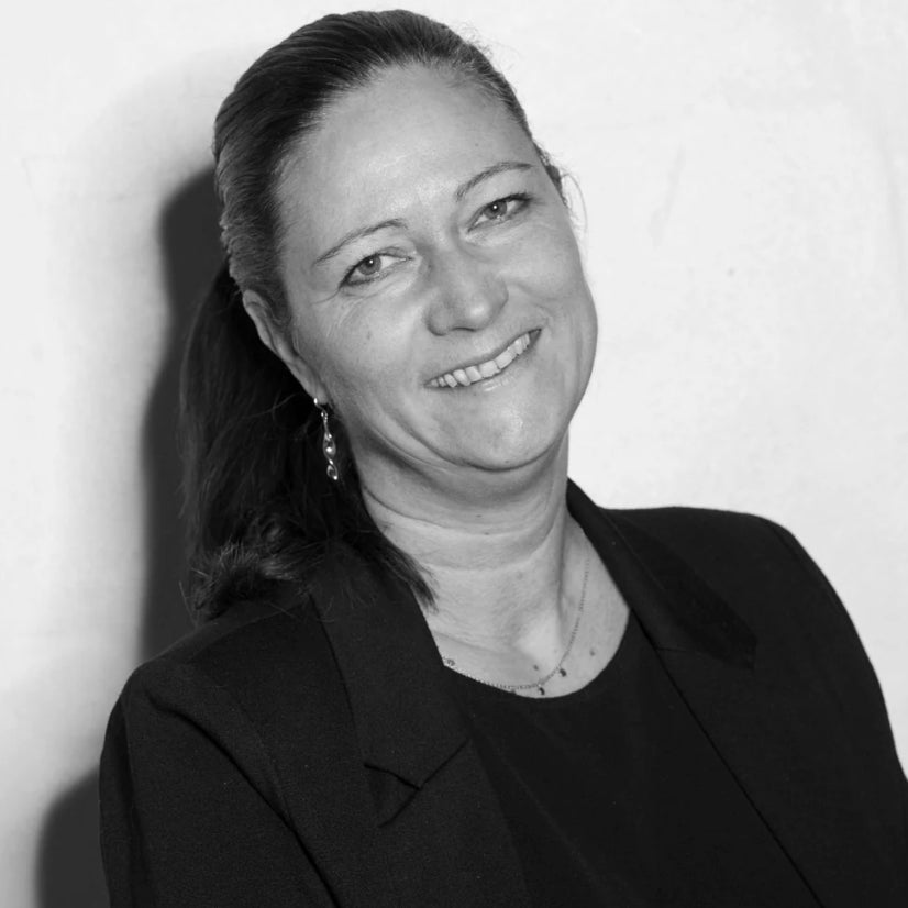 Frau mit braunen Haaren in schwarzer Kleidung lächelt vor neutralem Hintergrund.