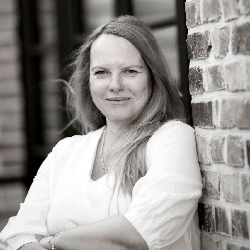 Frau mit langen Haaren lehnt entspannt an einer Ziegelwand.