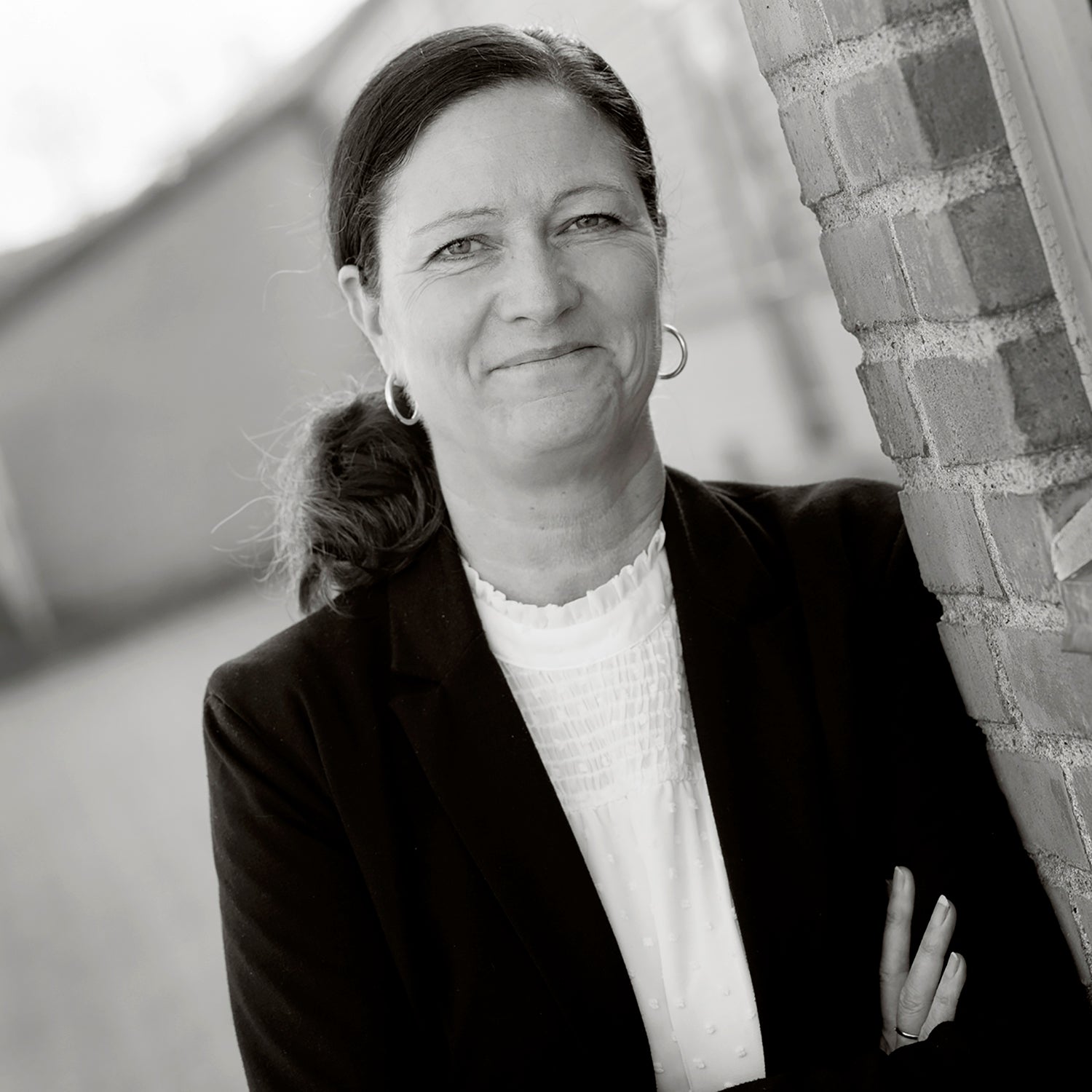 Frau mit dunkler Jacke lehnt an Ziegelwand, lächelt in die Kamera.