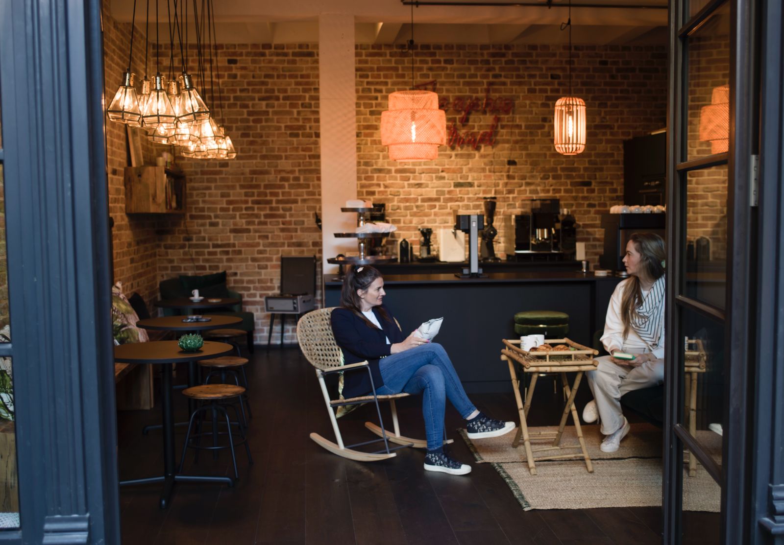 Zwei Frauen sitzen in einem Café mit Backsteinwänden, eine liest ein Buch.
