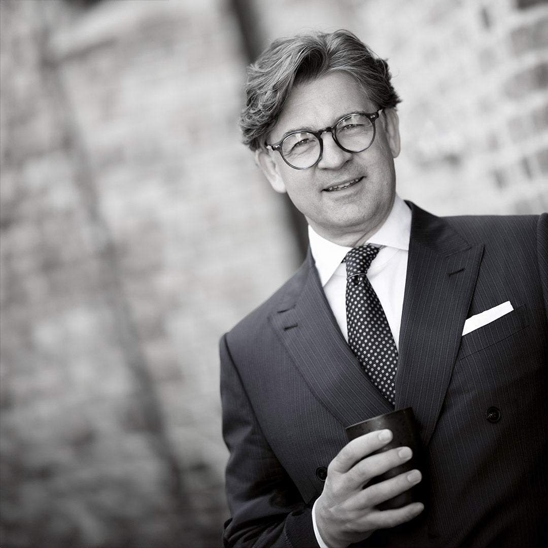 Mann im Anzug mit Brille lehnt an einer Ziegelmauer.