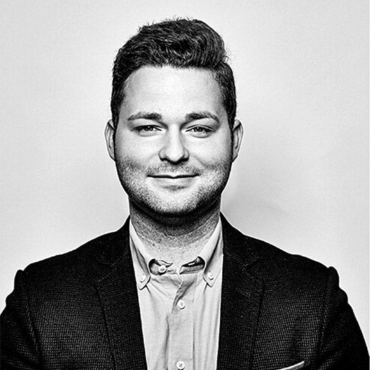 Mann trägt ein helles Hemd und dunkles Sakko und blickt direkt in die Kamera.